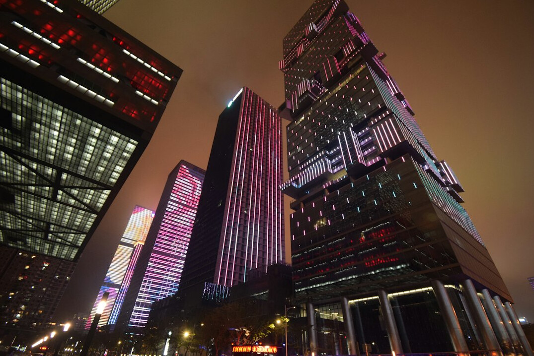 Multiple monitors displaying stock market candlestick charts with city skyline at dusk