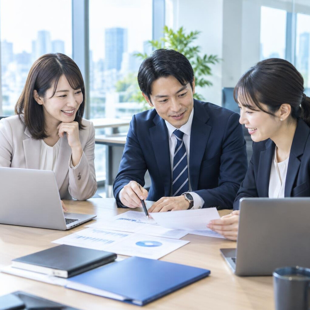 Japanese colleagues collaborating around a table with laptops in a bright office
